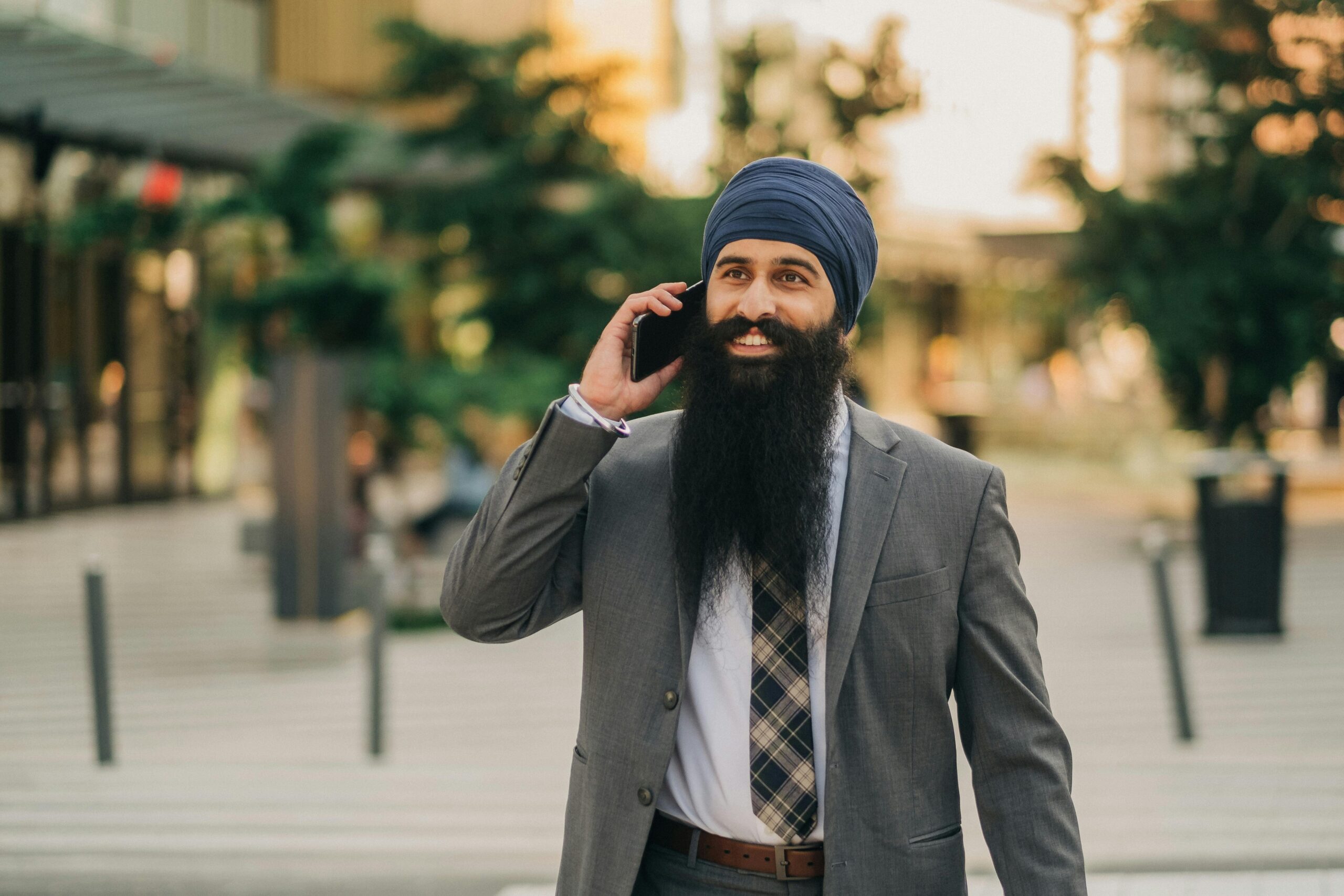 Smiling businessman with a turban talking on smartphone outdoors, showcasing confidence and professionalism.